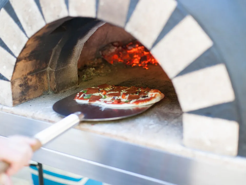 Pizza wird mit einem Pizzaschieber in einen Steinofen geschoben